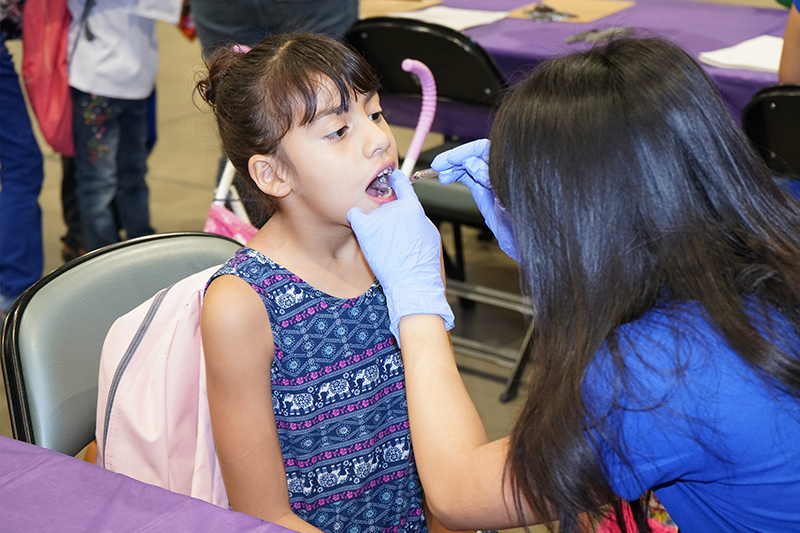 Oral health professional checking the inside of a young girl's mouth during a volunteer event 