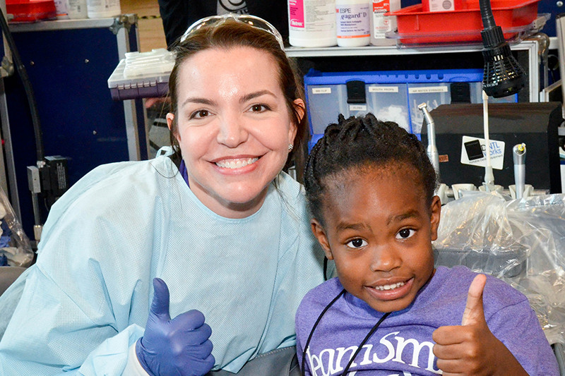 dentist and young girl smiling and giving a thumbs up at an oral health volunteer event 