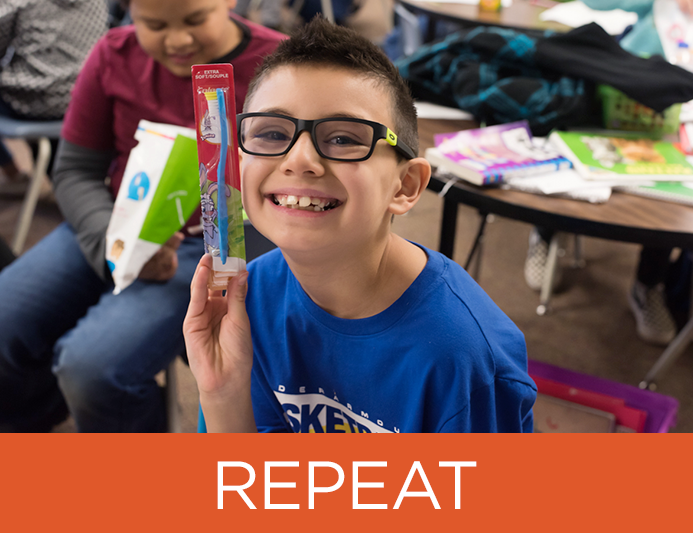 a young boy sitting down wearing glasses smiles as he holds up a toothbrush 