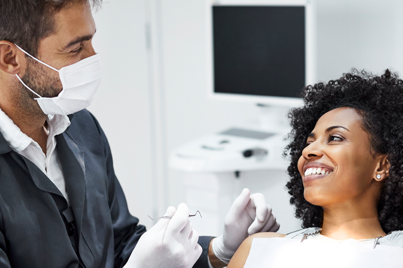 Smiling woman reclines back in dentist chair as the dentist prepares to take a look at her teeth with his instruments 