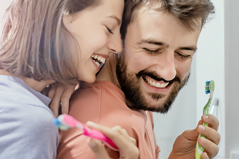 Smiling couple improving their oral health by brushing their teeth in the bathroom together