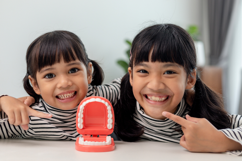 Two young girls smile while pointing at a fake mouth mold